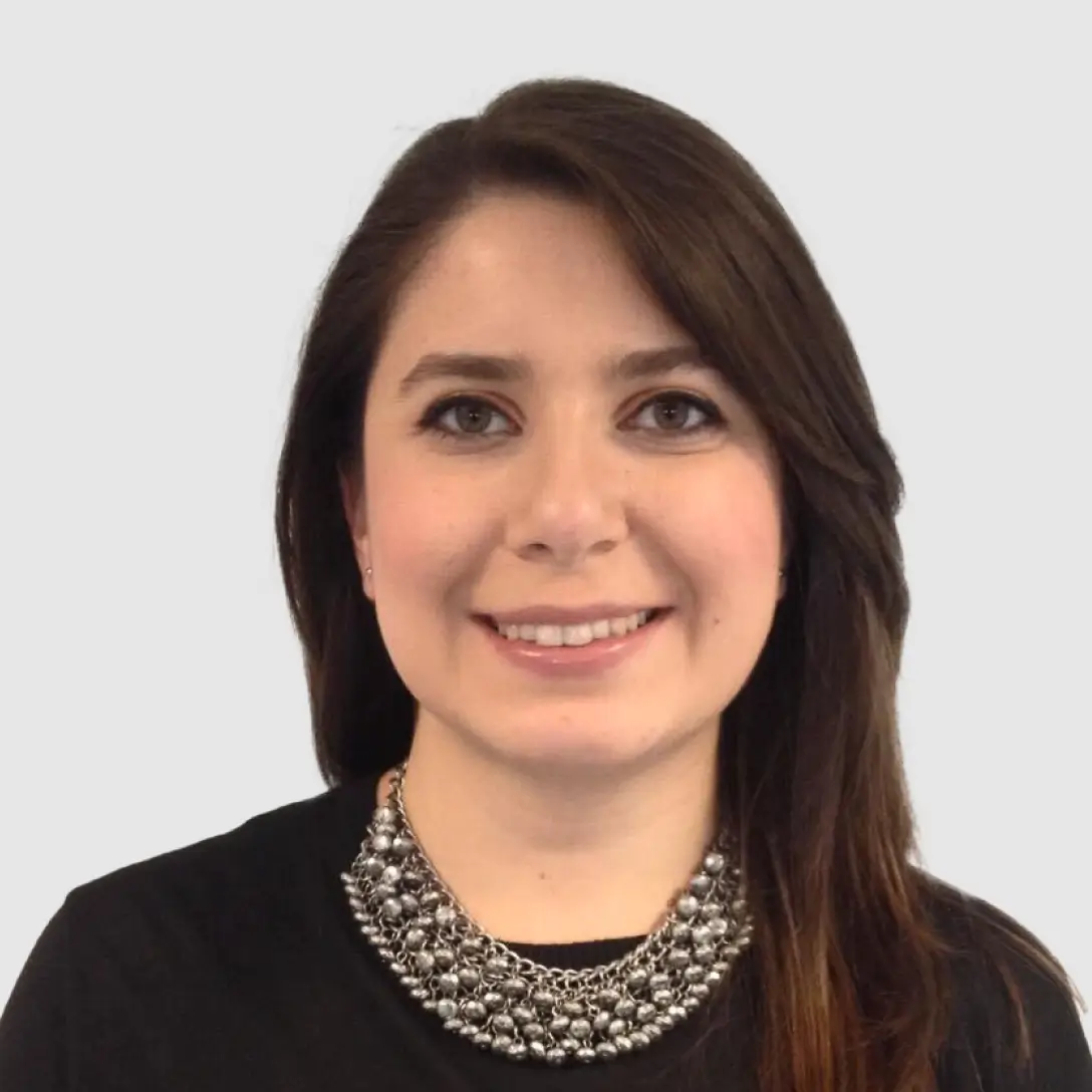 Portrait of a woman teacher with medium-length dark hair, looking confident and approachable, with a solid soft colored background